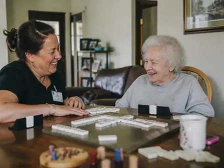 Cuidadora e idosa sorrindo durante jogo de mesa